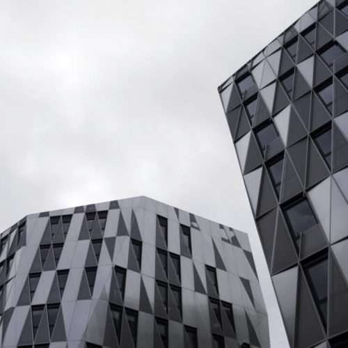 bottom-view-of-modern-unique-building-with-triangle-shaped-windows-of-black-color-on-bright-cloudy-e1695971005517.jpg